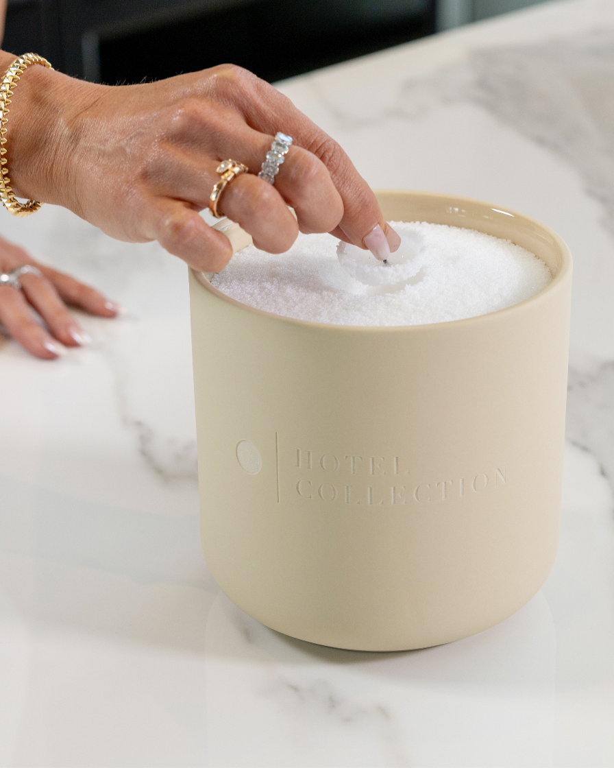 Beige container with soapy water on a marble surface, with hands interacting.