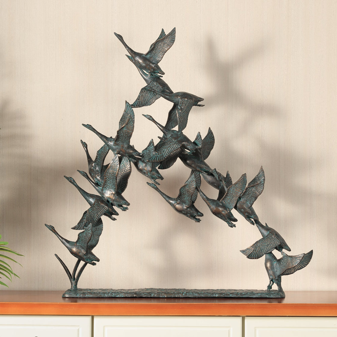 Bronze sculpture of geese flying in a circle on a wooden base.