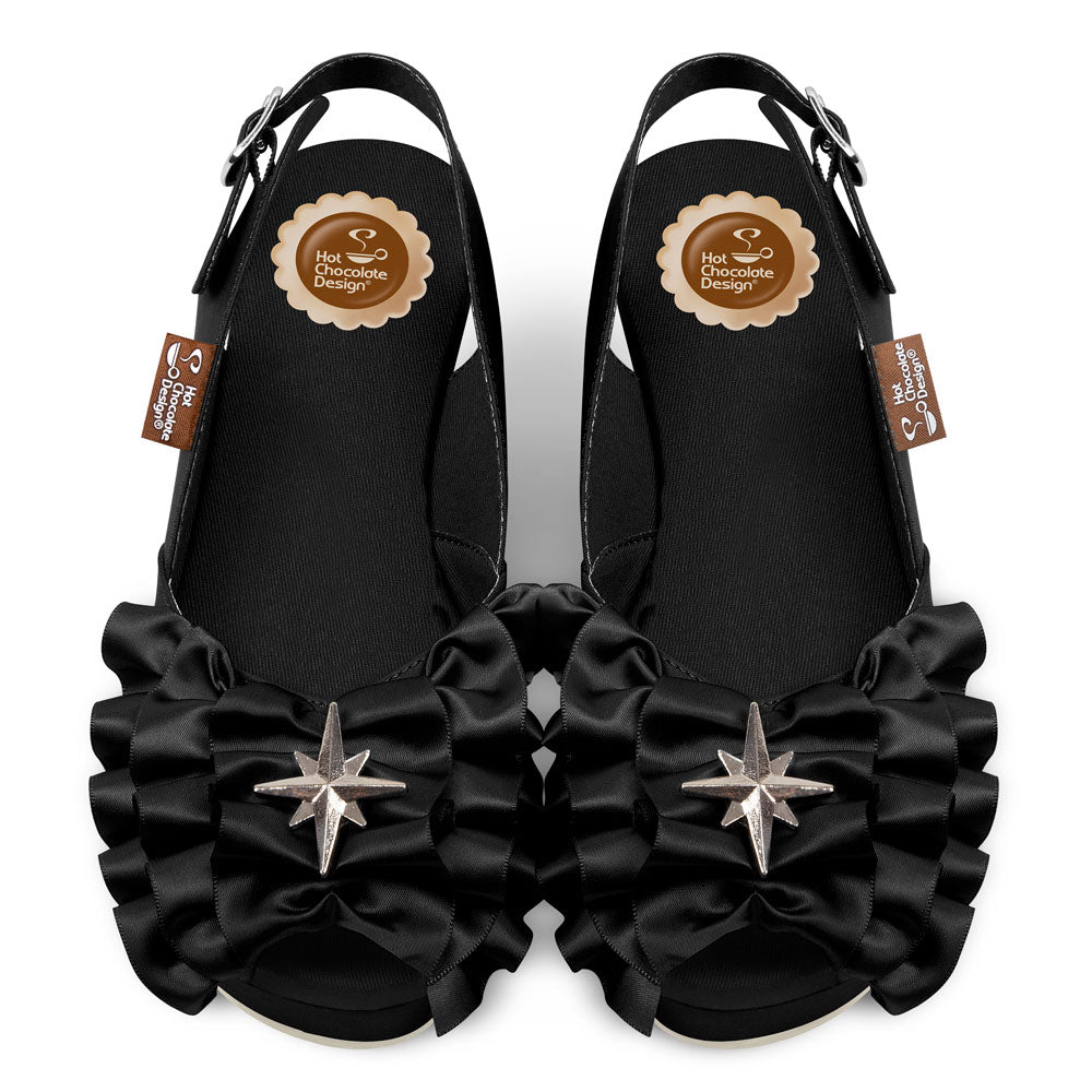 Black wedge sandals with ruffles and star embellishments on a white background