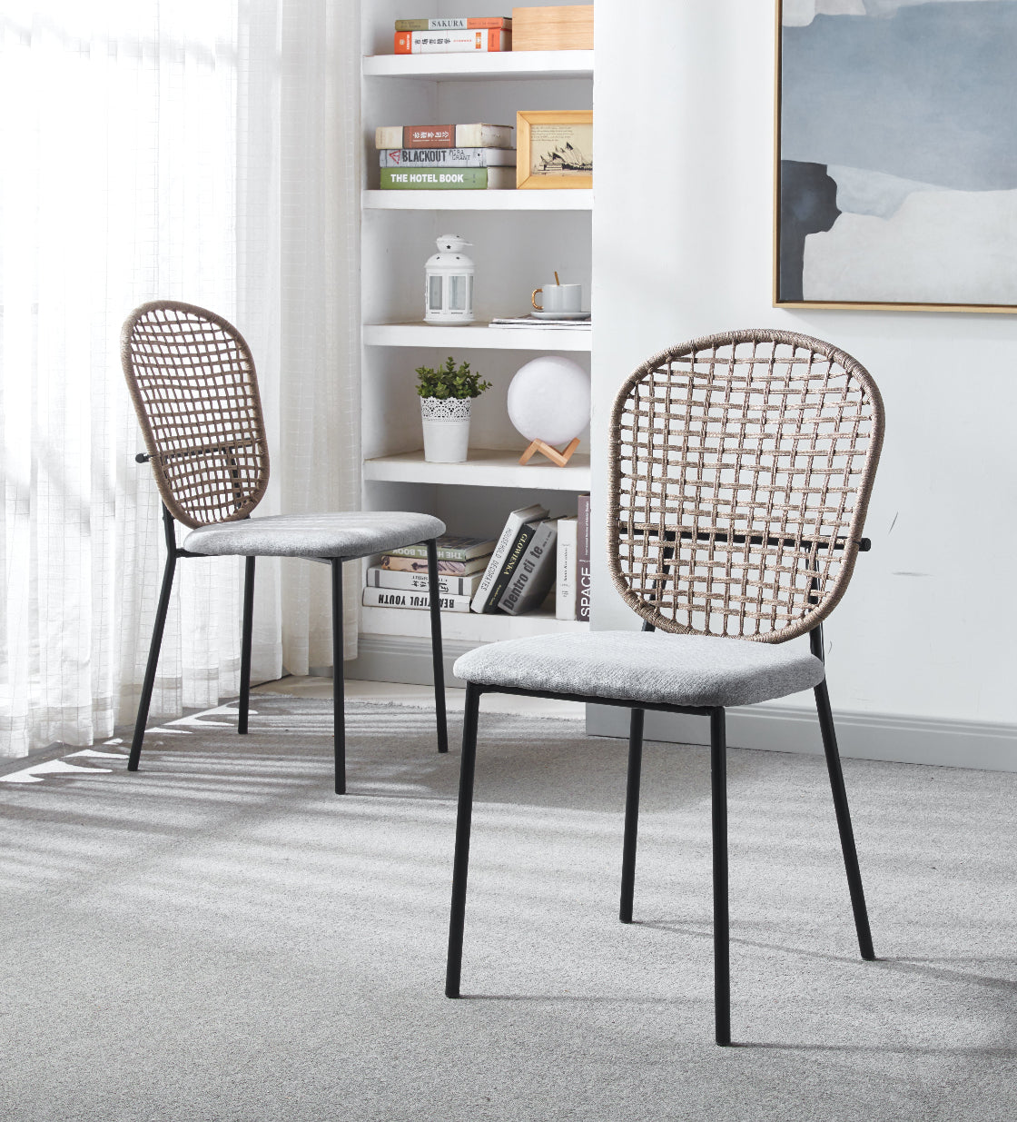 Two wicker-back chairs with black frames in a room with a bookshelf and decor.