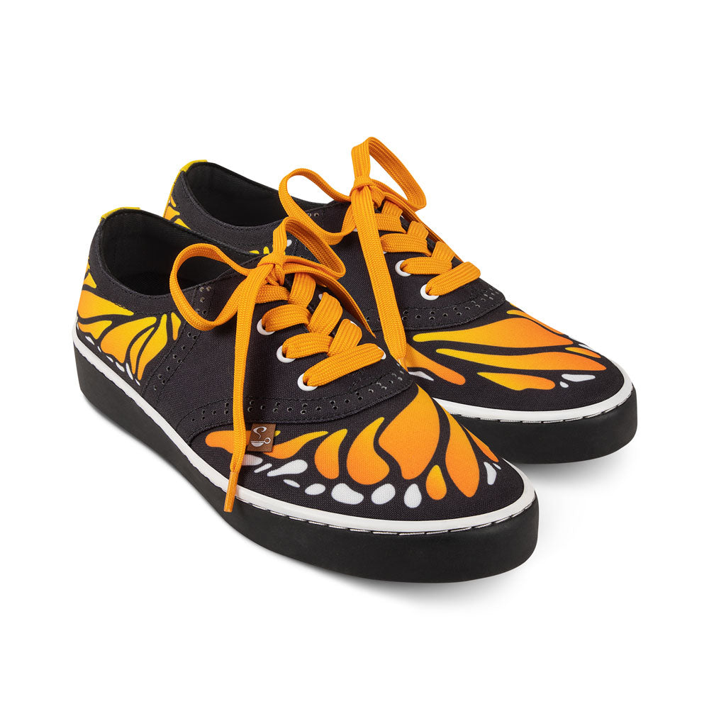 Black sneakers with orange butterfly design and matching laces on a white background