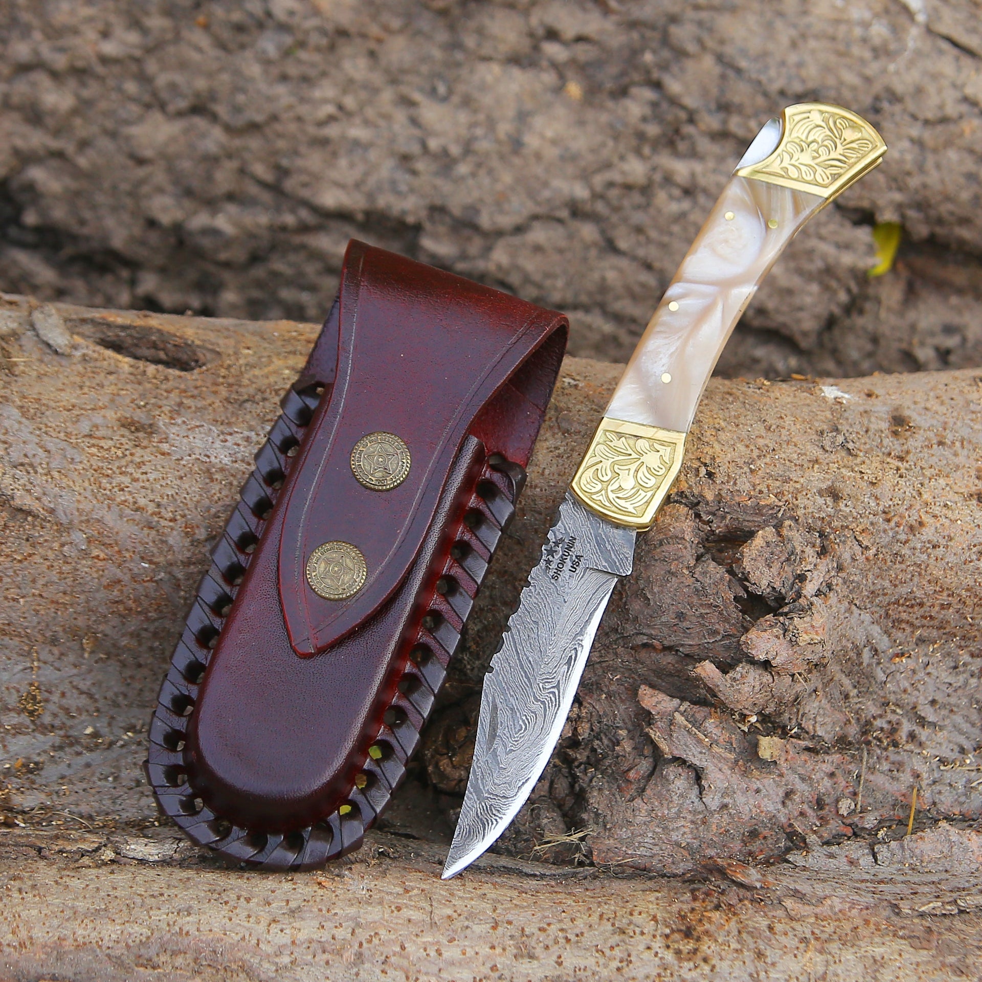 A handmade Damascus pocket knife with a leather sheath and mother of pearl resin handle, displaying the knife's blade and the intricate pattern of the Damascus steel.