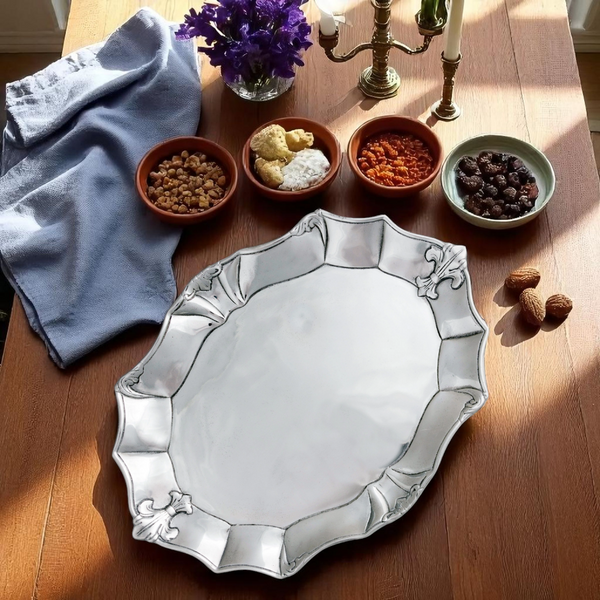 Decorative silver platter on a wooden table with bowls of food and a candlestick.