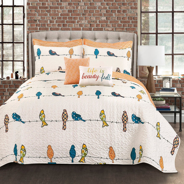 Bedding set with colorful bird pattern and 'life is beauty full' pillow on a bed in a room with brick wall and large windows.