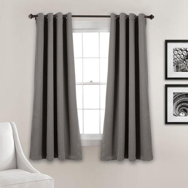 Gray curtains hanging in a room with a window and framed pictures on the wall.
