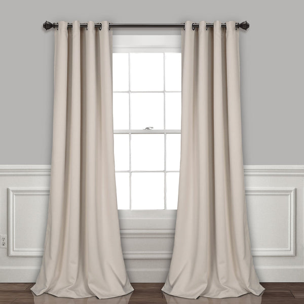 Beige curtains hanging on a window with a gray wall and white baseboard in the background.