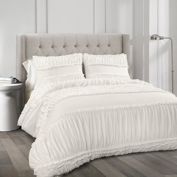 White ruffled bedding set on a bed with a gray upholstered headboard.