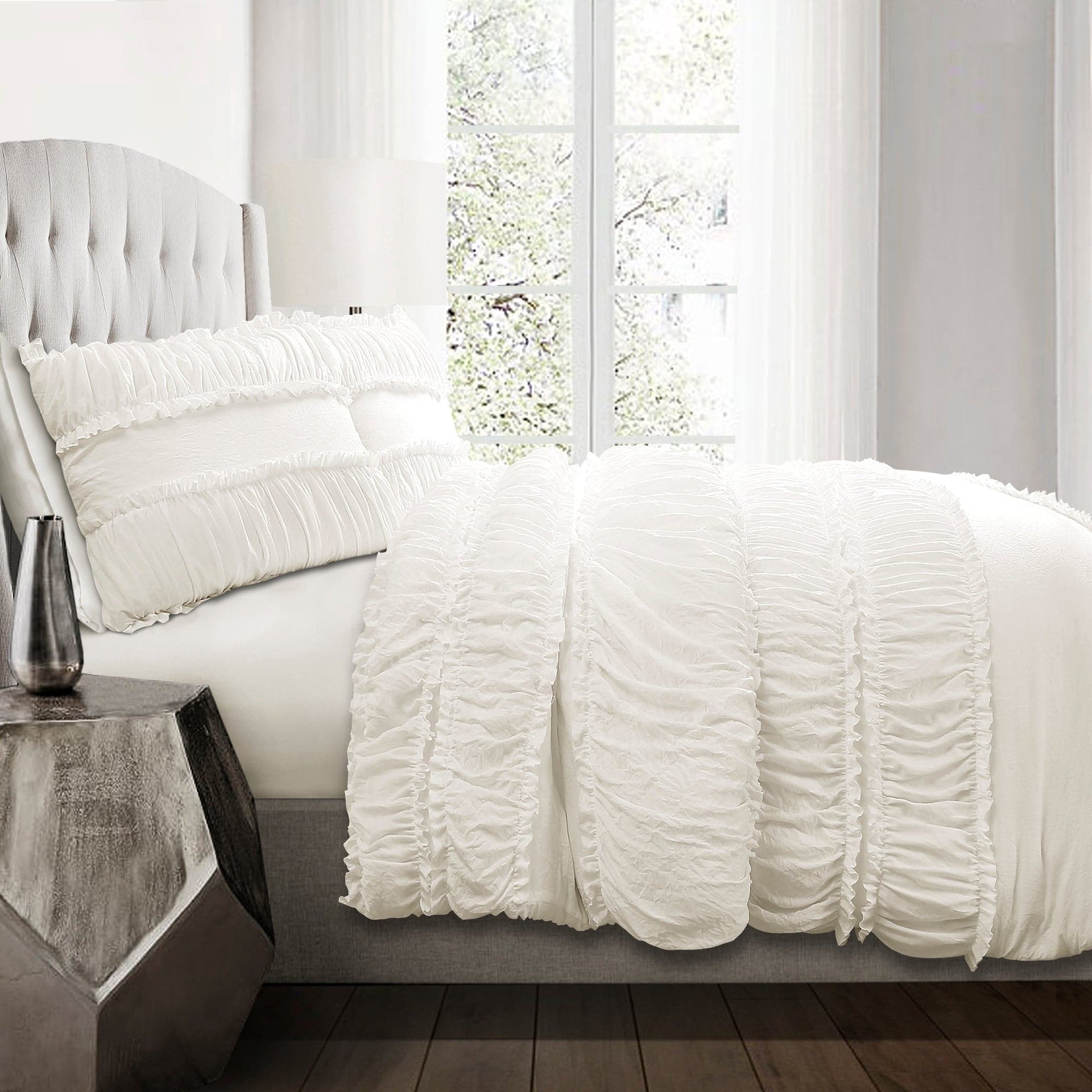 White textured bedding set on a bed in a bright bedroom with large windows.