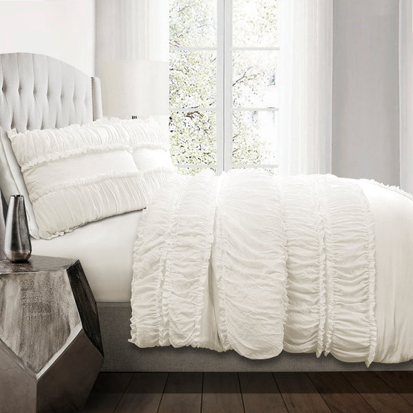 White textured bedding set on a bed in a bright bedroom with large windows.