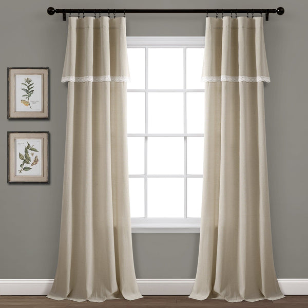 Beige curtains with lace trim hanging in front of a window with a gray wall and framed pictures in the background.
