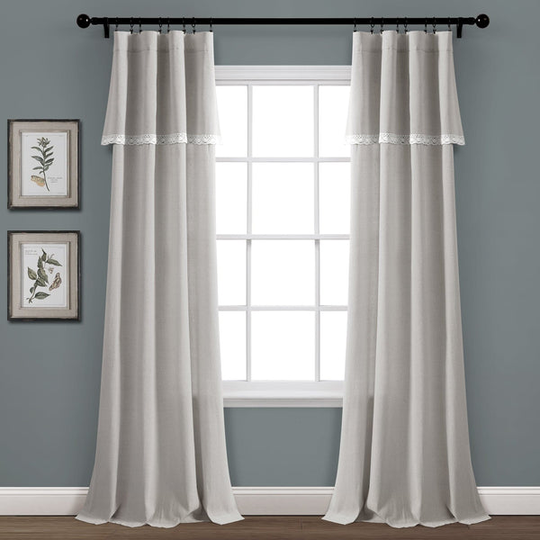 Sheer gray curtains with lace trim hanging in front of a window on a gray wall.