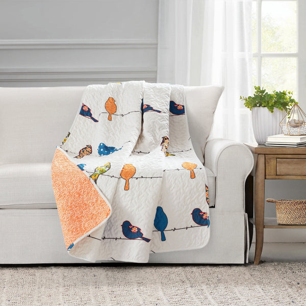 Decorative quilt with bird pattern draped over a sofa in a living room setting.