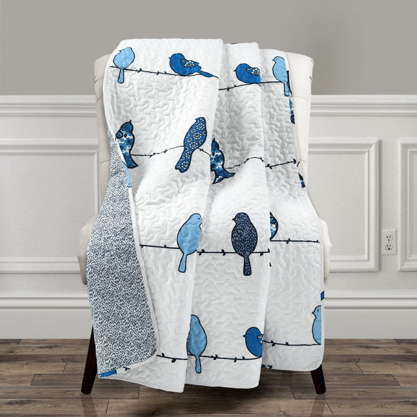 White quilt with blue bird pattern draped over a chair in a room.
