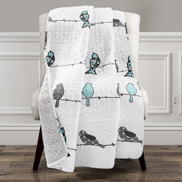 White quilt with bird pattern draped over a chair in a room.