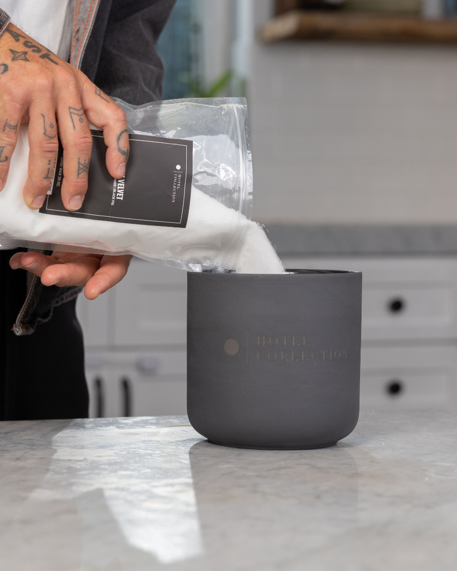 Person pouring coffee from a bag into a black container on a kitchen counter.