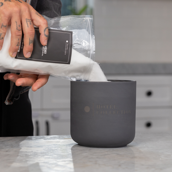 Person holding a package over a dark gray mug on a marble surface.