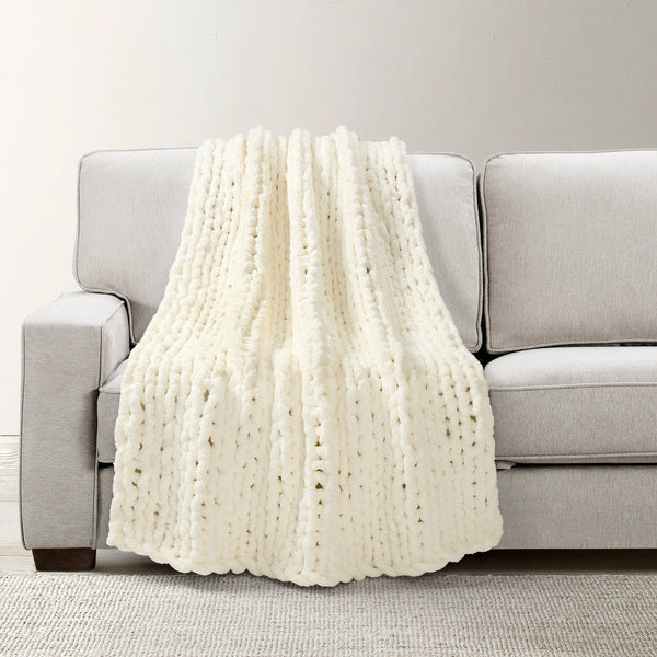 White knitted blanket draped over a gray sofa against a neutral background