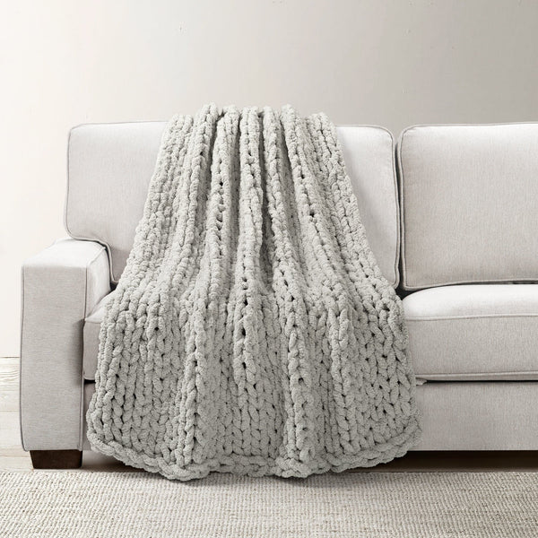Gray chunky knit blanket draped over a light gray sofa against a plain background