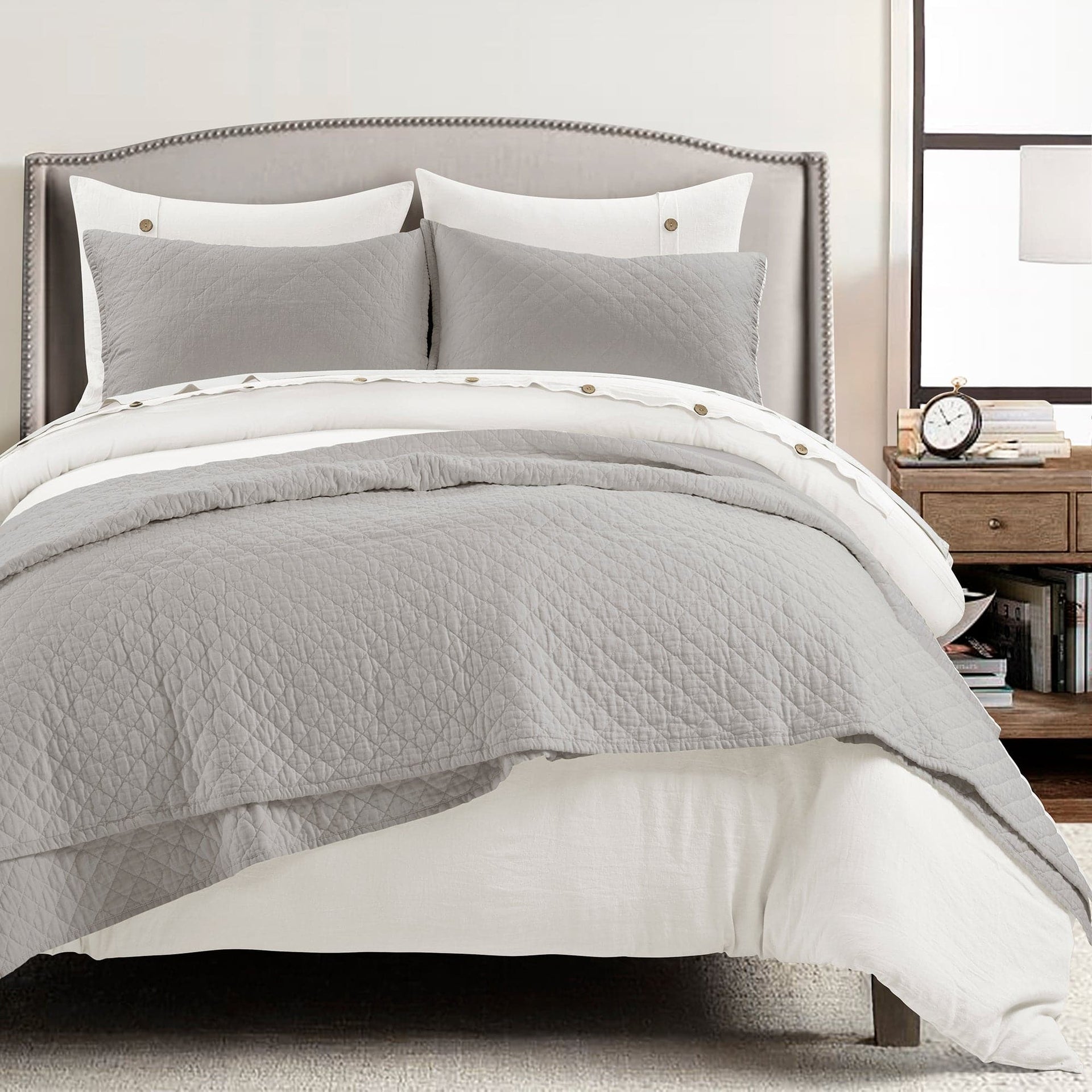 Gray quilted comforter set on a bed with pillows and a nightstand in the background.