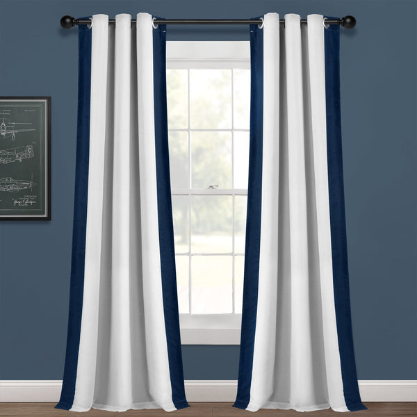 White curtains with navy blue accents hanging in front of a window with a dark blue wall and framed picture in the background.