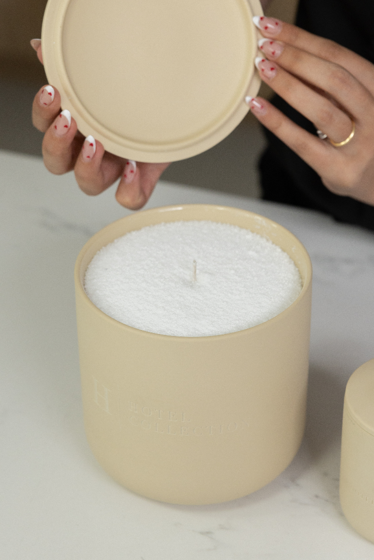 Beige candle with lid held by a hand on a light background