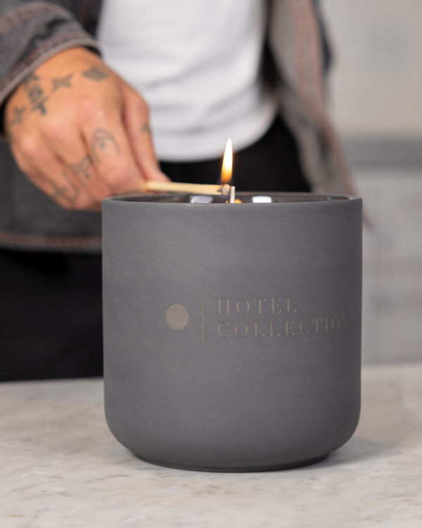Gray candle with 'Hotel Collection' branding being lit on a marble surface.