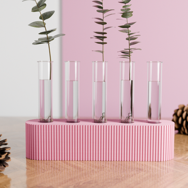 Clear glass vases with greenery on a pink striped stand against a pink background