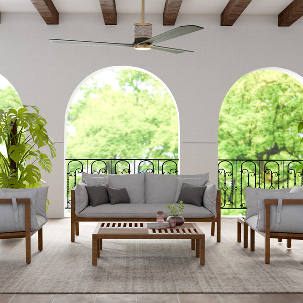 62″ Levant Ceiling Fan | Aged Brass - Outdoor patio with gray sofa, wooden coffee table, and chairs with cushions, surrounded by greenery.