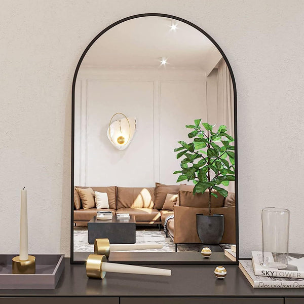 24x36 Inch Black Metal Framed Arched Wall Mirror reflecting a cozy living room with a tan sofa and indoor plant, placed on a black console table.