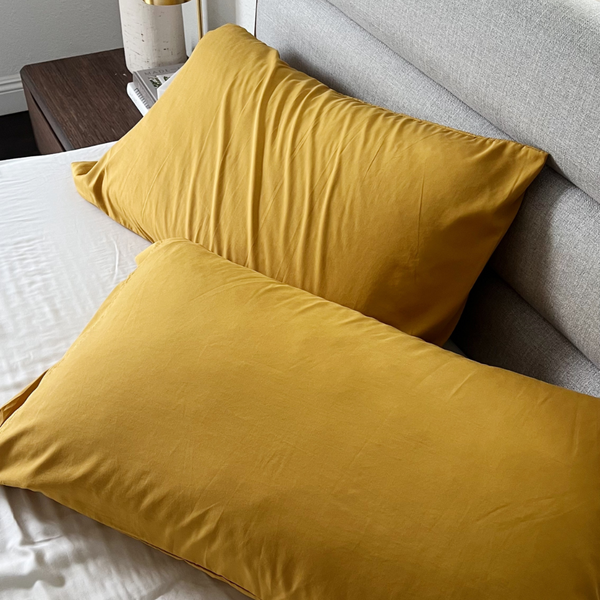 Two mustard yellow pillows on a bed with a neutral-colored headboard.