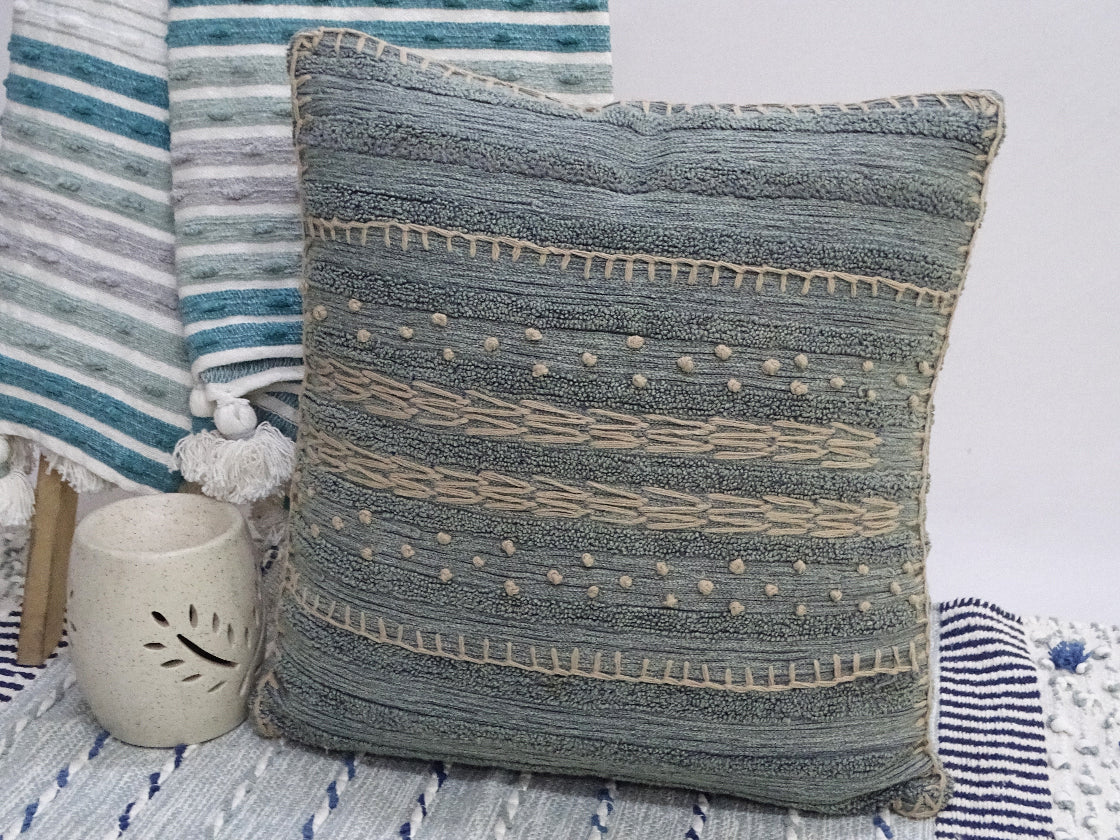 Textured blue pillow on a bed with striped bedding