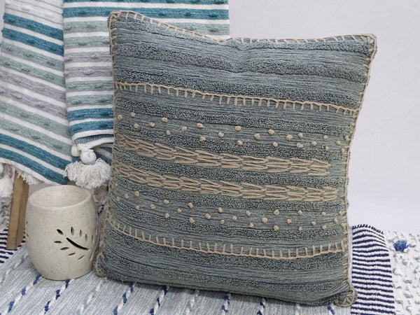 Textured blue pillow on a bed with striped bedding