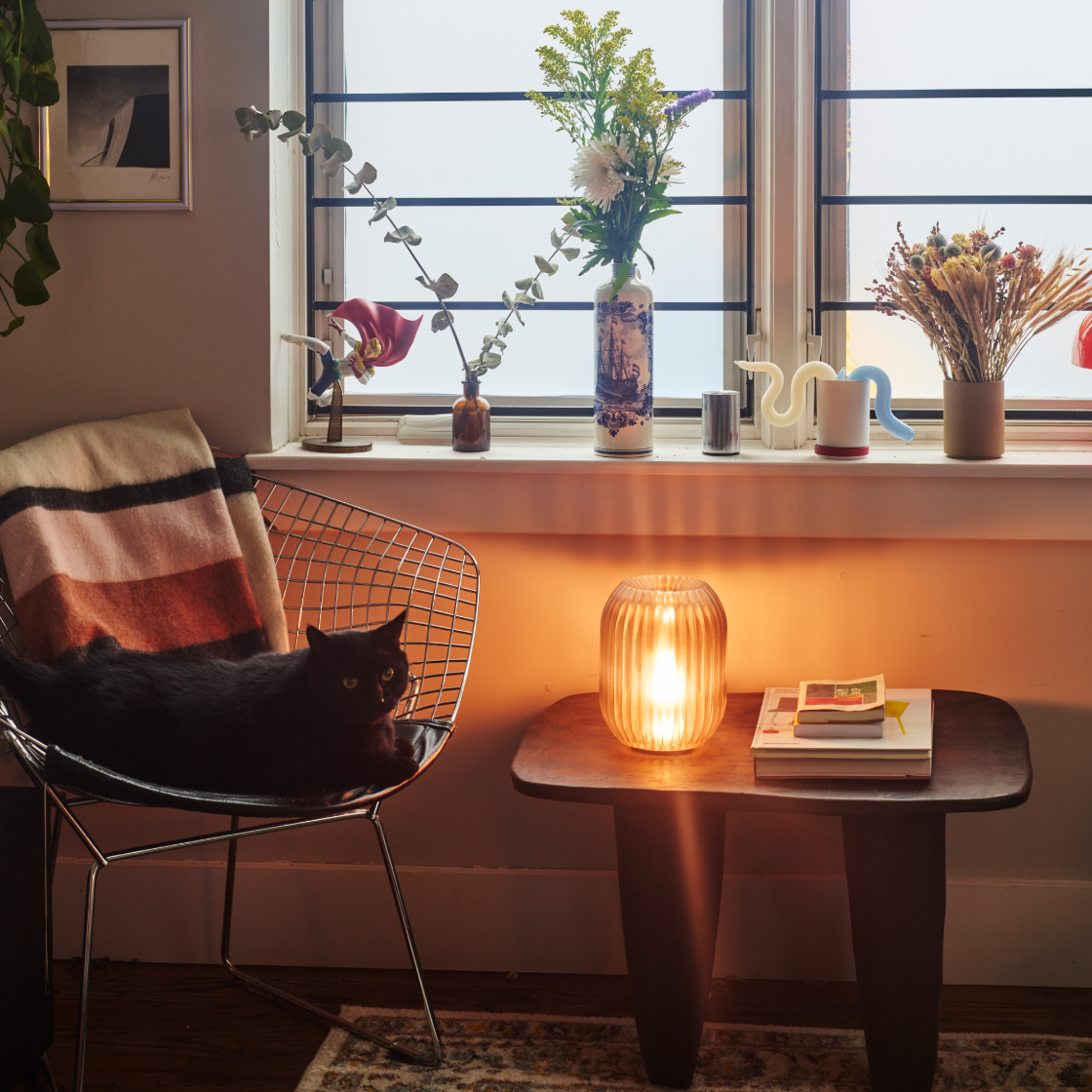Cozy living room with a cat on a chair, a table with a candle, and decorative items by a window.