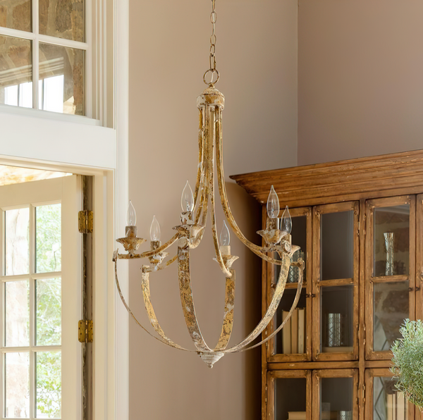Gold chandelier hanging in a room with a wooden cabinet and window.