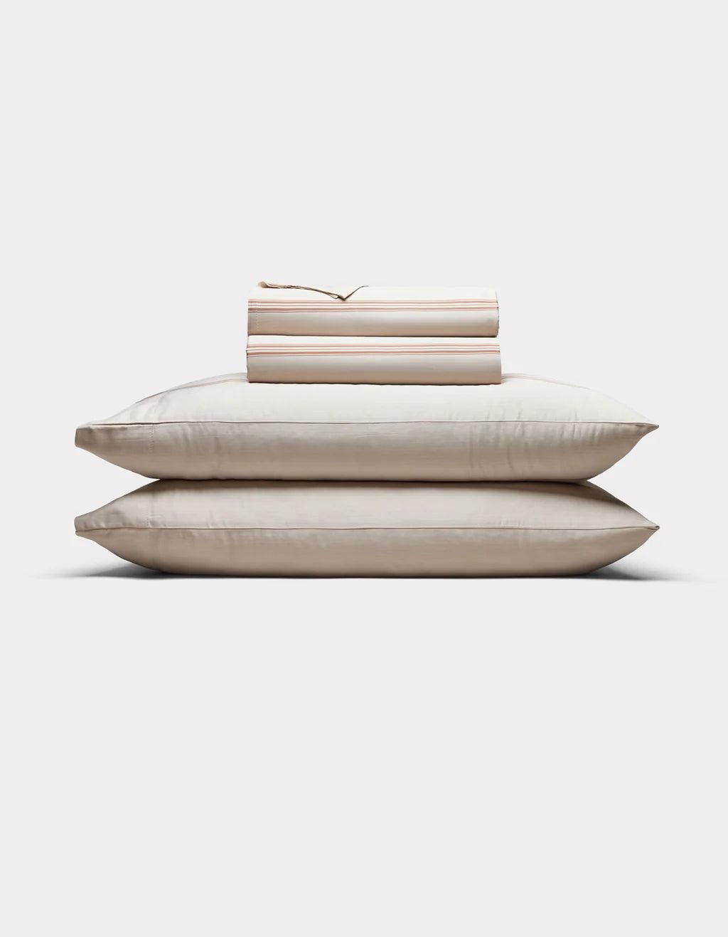 Baja Stripe in Maple - Stack of beige pillows and bed sheets on a white background