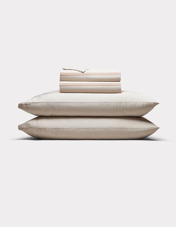 Baja Stripe in Maple - Stack of beige pillows and bed sheets on a white background