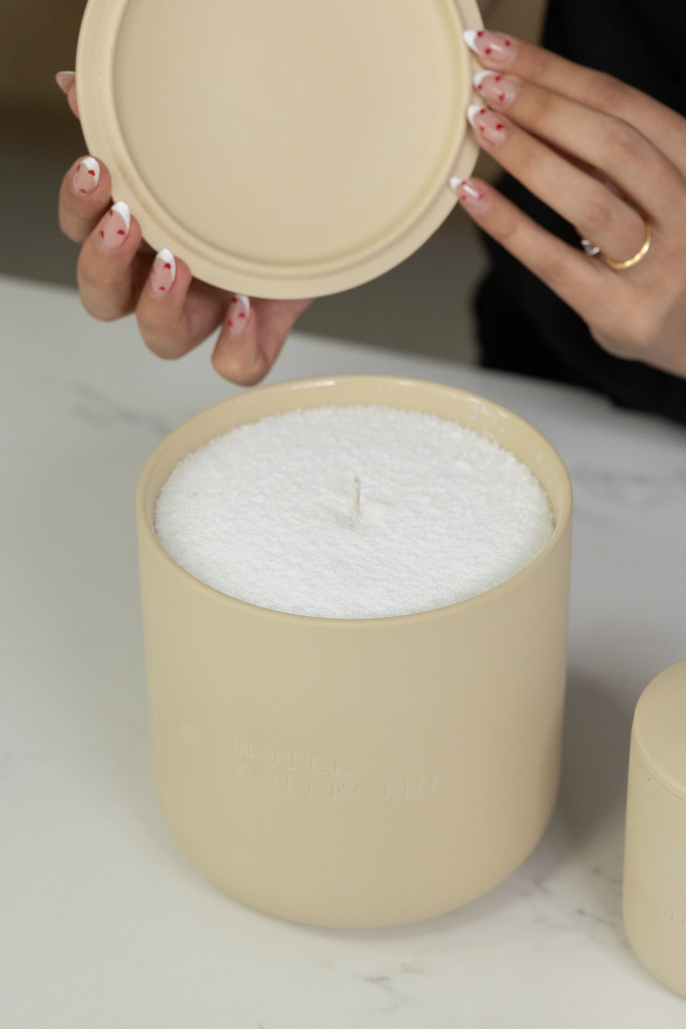  Beige candle with lid held by a hand on a light background