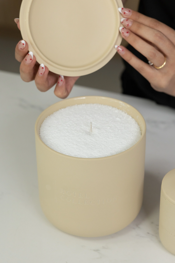  Beige candle with lid held by a hand on a light background