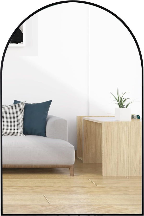 24x36 Inch Black Metal Framed Arched Wall Mirror mounted above a light wood console in a modern living room with a gray sofa and accent pillows.
