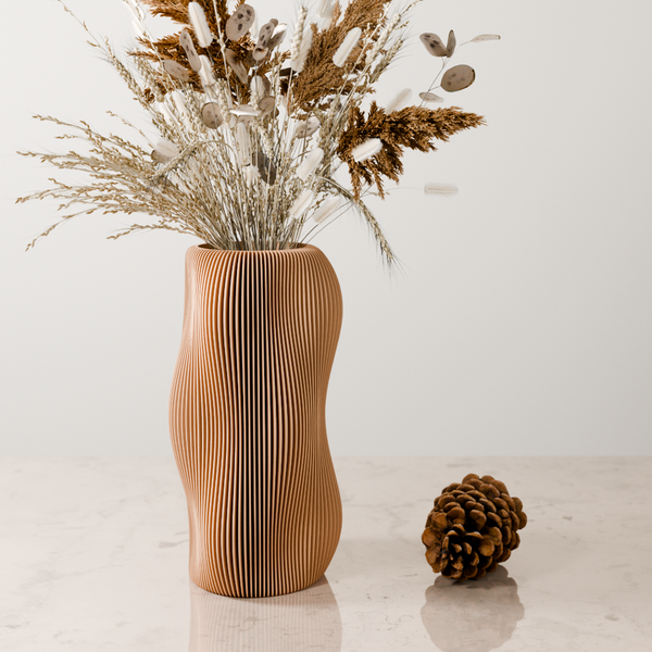 Wooden vase with wavy design holding dried flowers on a light surface.