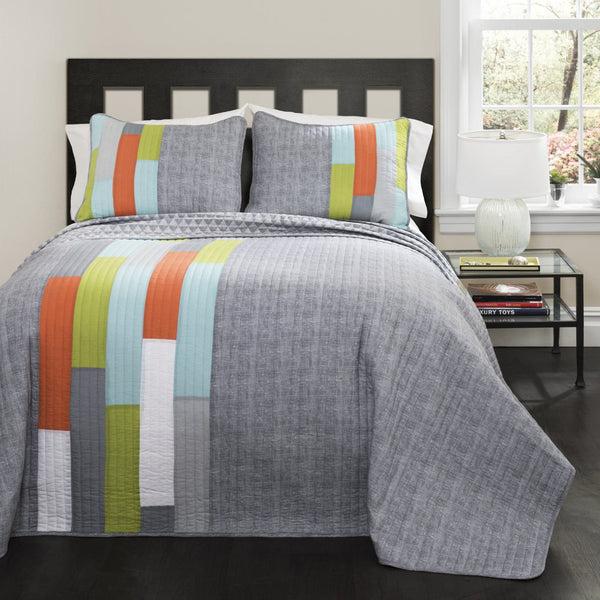 Gray quilt with colorful stripes on a bed in a room with a window and side table.