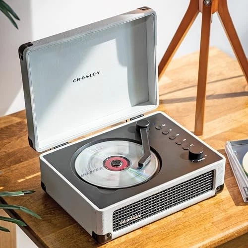 Crosley record player on a wooden surface with a plant and tripod in the background