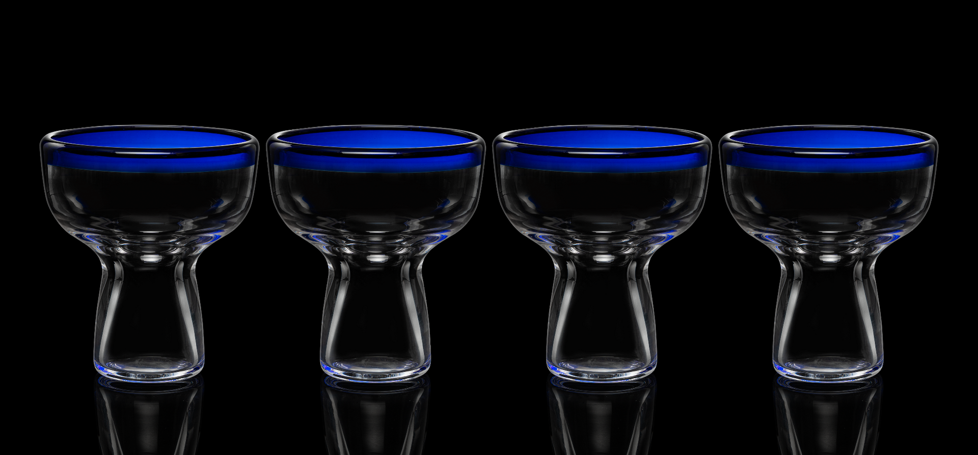 Four clear glass tumblers with blue interior on a black background