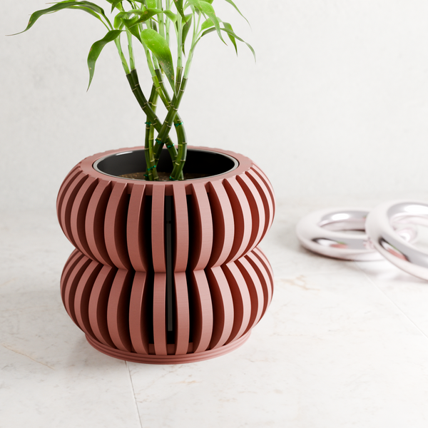 Decorative pink and white striped planter with a plant on a light surface.