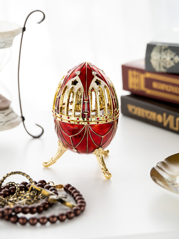Decorative red egg with gold intricate design on a white surface with books and jewelry.