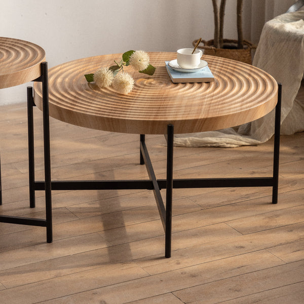 Round wooden coffee table with black metal legs on a wooden floor.