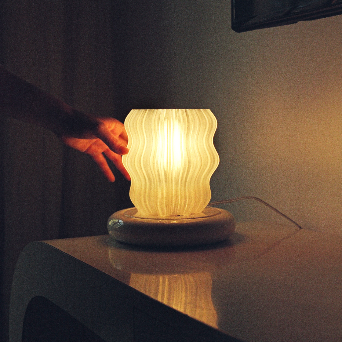 Hand reaching towards a wavy-patterned lamp on a surface with a dark background