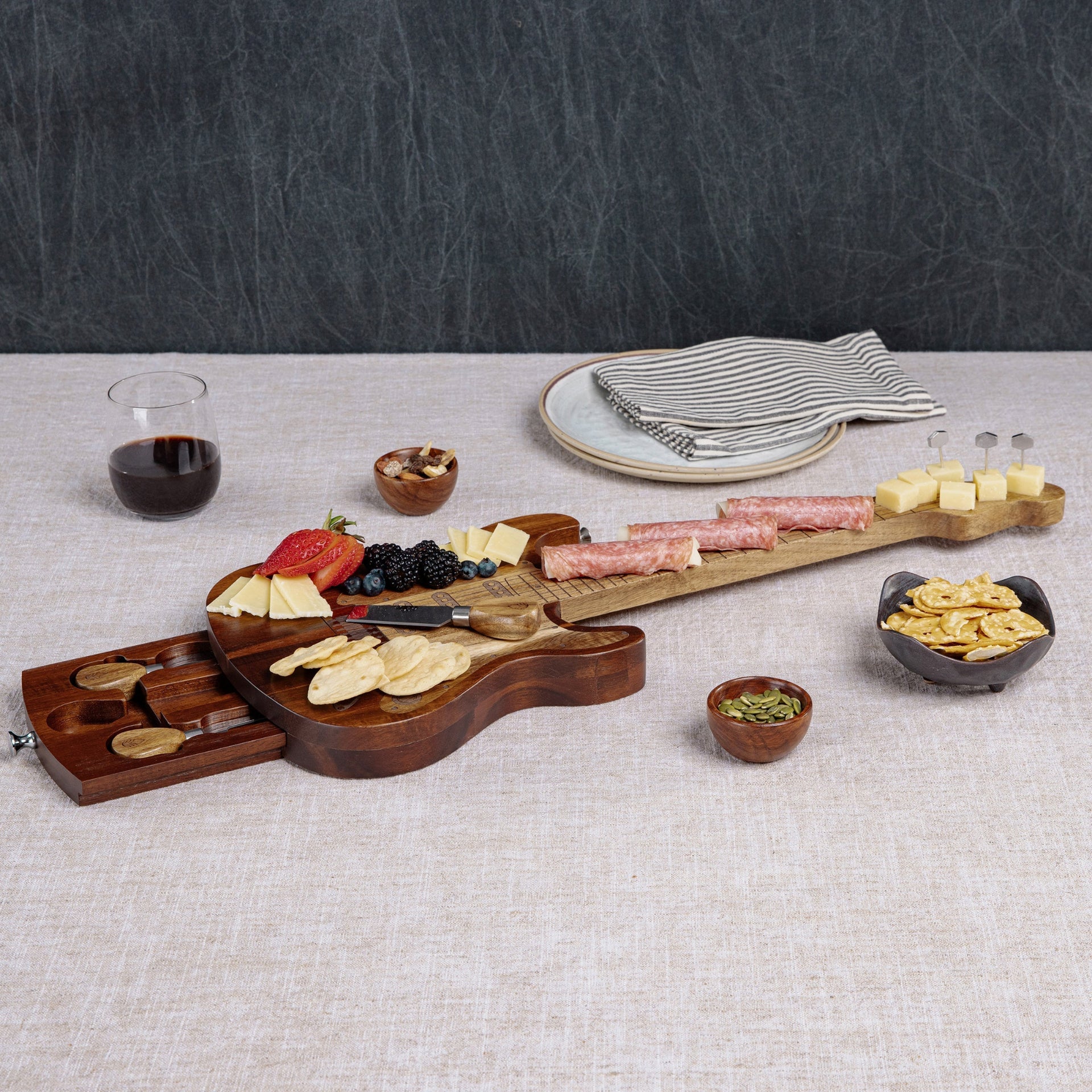 Wooden cheeseboard with assorted foods on a textured surface