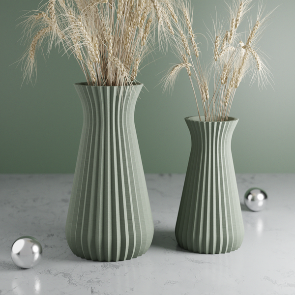 Two green ribbed vases with dried plants on a marble surface against a green wall.