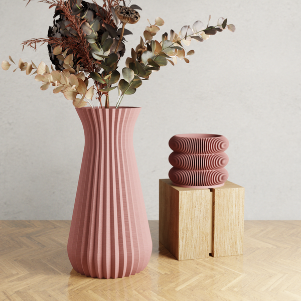Pink ribbed vase with dried plants on a wooden surface